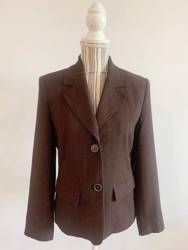 May include: A brown blazer with thin white stripes. The blazer has a notched collar, two button closure, and a single pocket on the left side.