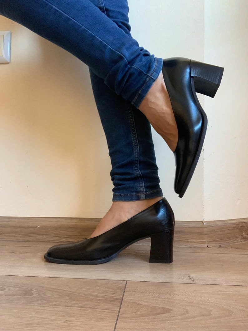 May include: Black leather pumps with a square toe and a block heel. The shoes are worn with blue jeans. The heels are approximately 3 inches high.
