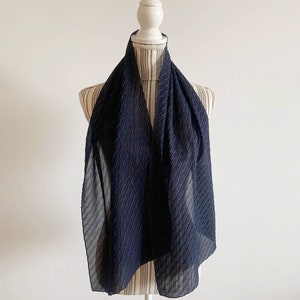 May include: A black sheer scarf with a textured pattern. The scarf is draped over a white mannequin.