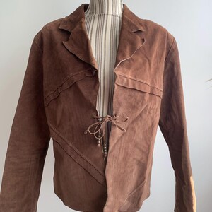 May include: A brown suede jacket with a tie closure and a unique asymmetrical design.
