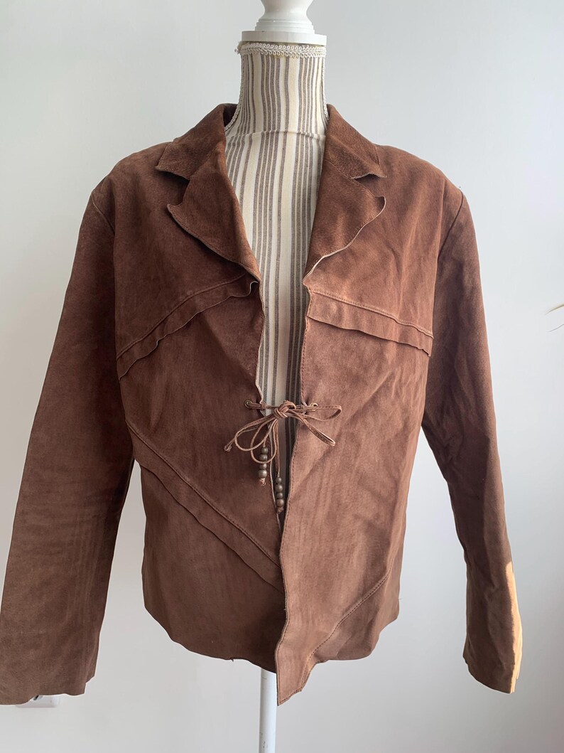 May include: A brown suede jacket with a tie closure and a unique asymmetrical design.