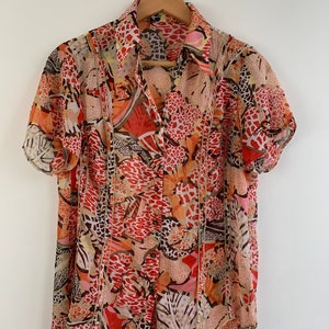 Pode incluir: Uma camisa de botões de manga curta com um padrão de estampa animal colorido em tons de laranja, marrom e branco.
