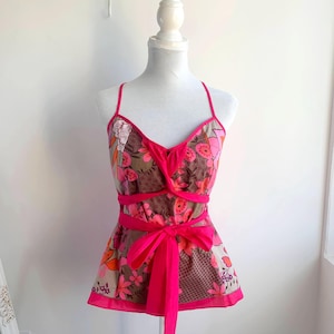 Könnte beinhalten: Ein Oberteil mit floralem Muster und einer rosa Schleife. Das Oberteil hat einen Neckholder-Ausschnitt und ein Wickeldesign. Der Stoff hat ein braunes, rosa und orangefarbenes Blumenmuster mit rosa Besatz. Die Schleife ist leuchtend rosa.