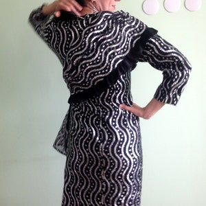 May include: A black and silver sequined dress with a ruffled neckline and long sleeves. The dress has a wavy pattern.