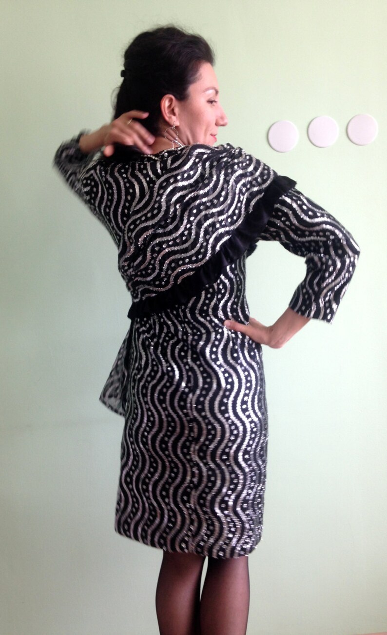 May include: A black and silver sequined dress with a ruffled neckline and long sleeves. The dress has a wavy pattern.