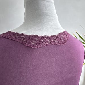 May include: A plum-colored top with a delicate lace trim along the neckline. The top is displayed on a white mannequin, showcasing the scoop neckline and the texture of the lace. The fabric appears soft and drapes smoothly.