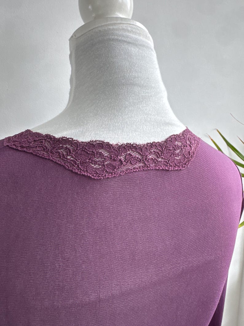 May include: A plum-colored top with a delicate lace trim along the neckline. The top is displayed on a white mannequin, showcasing the scoop neckline and the texture of the lace. The fabric appears soft and drapes smoothly.