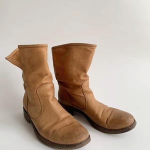 May include: A pair of brown leather ankle boots with a slouchy look. The boots have a rounded toe and a low heel.