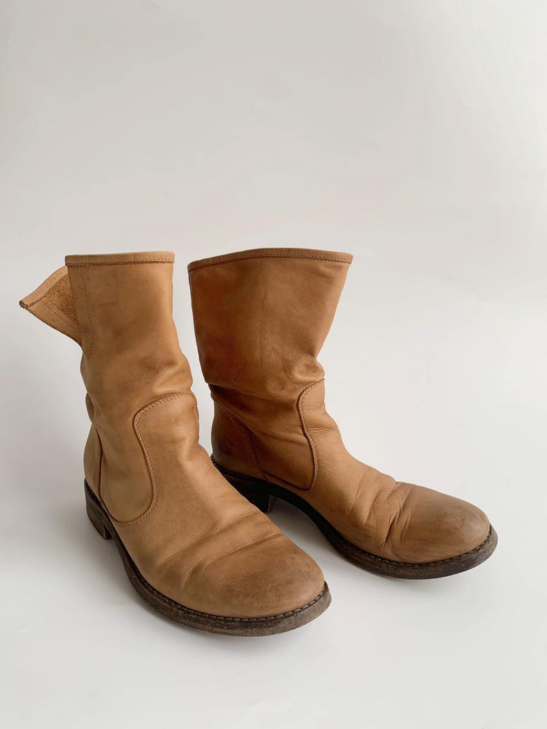May include: A pair of brown leather ankle boots with a slouchy look. The boots have a rounded toe and a low heel.