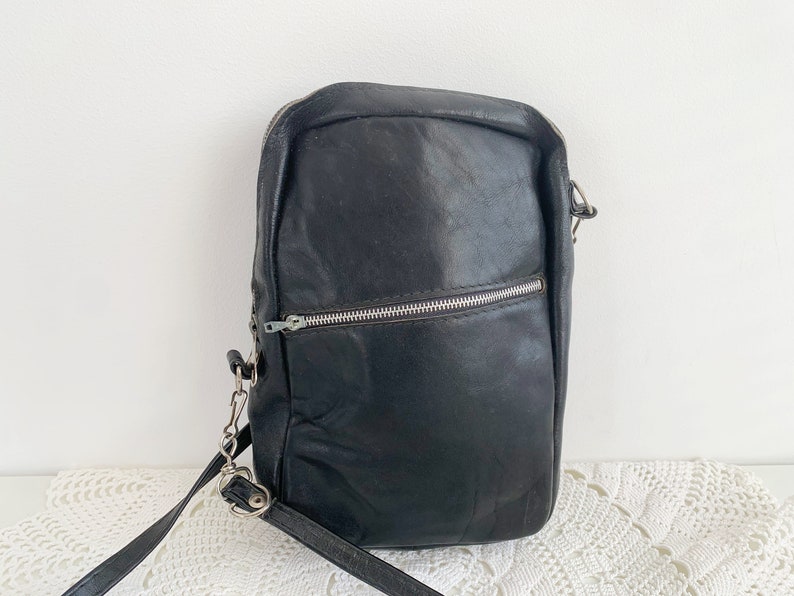 Pu&ograve; includere: Una borsa a tracolla in pelle nera con una cerniera argentata e una lunga tracolla regolabile.