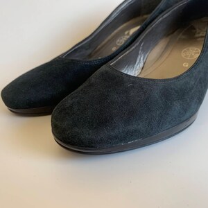 May include: A pair of black suede heeled shoes with a black rubber sole.