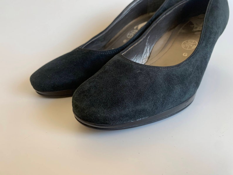 May include: A pair of black suede heeled shoes with a black rubber sole.