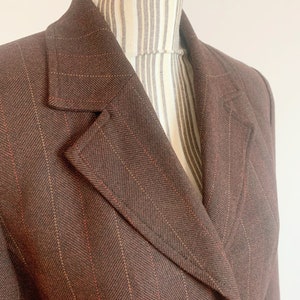 May include: A brown blazer with thin red and white stripes. The blazer has a single button closure and a notched collar.