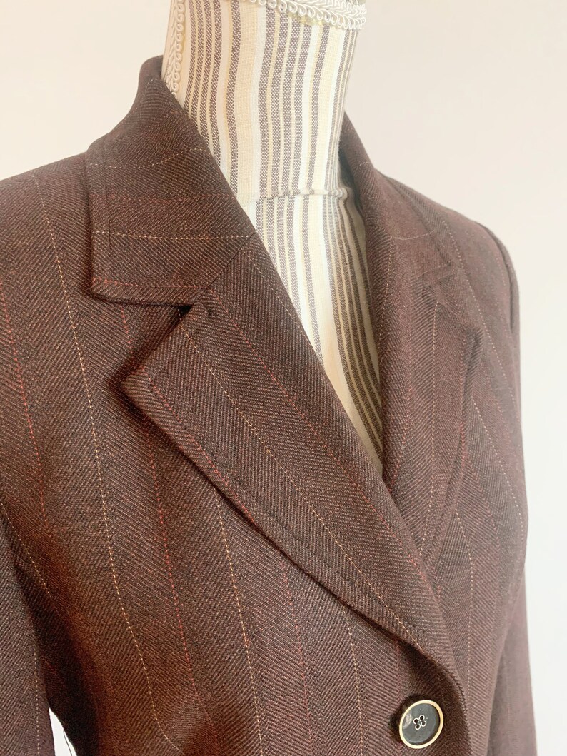 May include: A brown blazer with thin red and white stripes. The blazer has a single button closure and a notched collar.