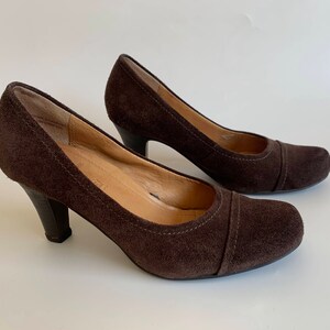 May include: A pair of brown suede heeled pumps with a closed toe and a rounded toe shape.
