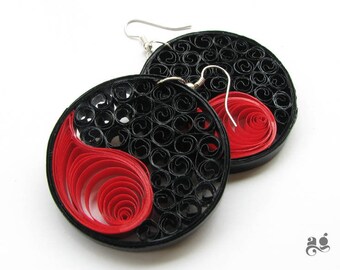 Può includere: Un paio di orecchini yin yang neri e rossi realizzati con quilling di carta. Gli orecchini sono rotondi e hanno un gancio argentato.