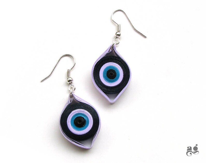 May include: A pair of earrings with a purple and black evil eye design. The earrings are made of paper and have silver hooks.