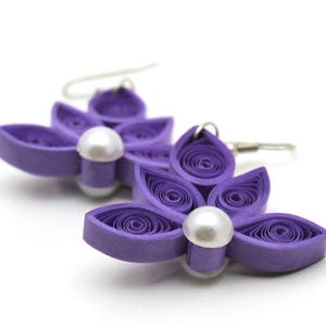 Pu&ograve; includere: Orecchini a forma di fiore di carta viola con un accento di perla. Gli orecchini sono realizzati in carta arricciata e hanno un aspetto delicato e femminile.
