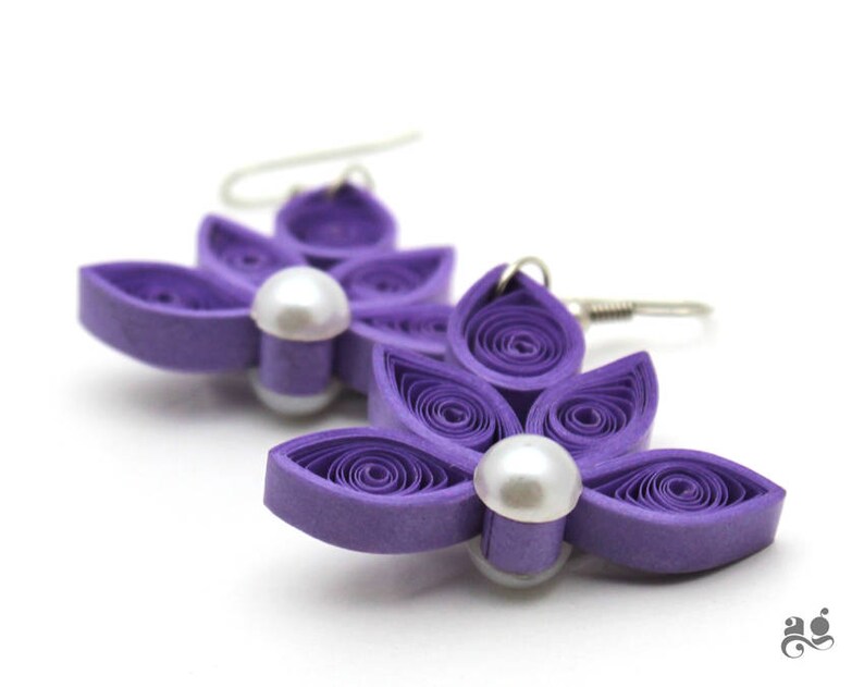 Pu&ograve; includere: Orecchini a forma di fiore di carta viola con un accento di perla. Gli orecchini sono realizzati in carta arricciata e hanno un aspetto delicato e femminile.