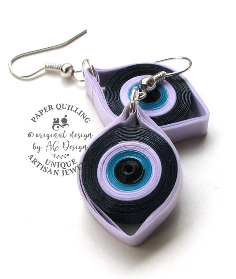 May include: A pair of purple and black evil eye earrings made with paper quilling. The earrings are handmade and feature a silver hook.