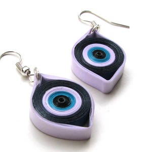 May include: A pair of silver earrings with a purple and blue eye design. The earrings are made of paper and are shaped like a teardrop.