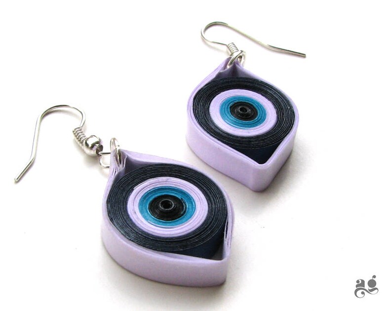 May include: A pair of silver earrings with a purple and blue eye design. The earrings are made of paper and are shaped like a teardrop.