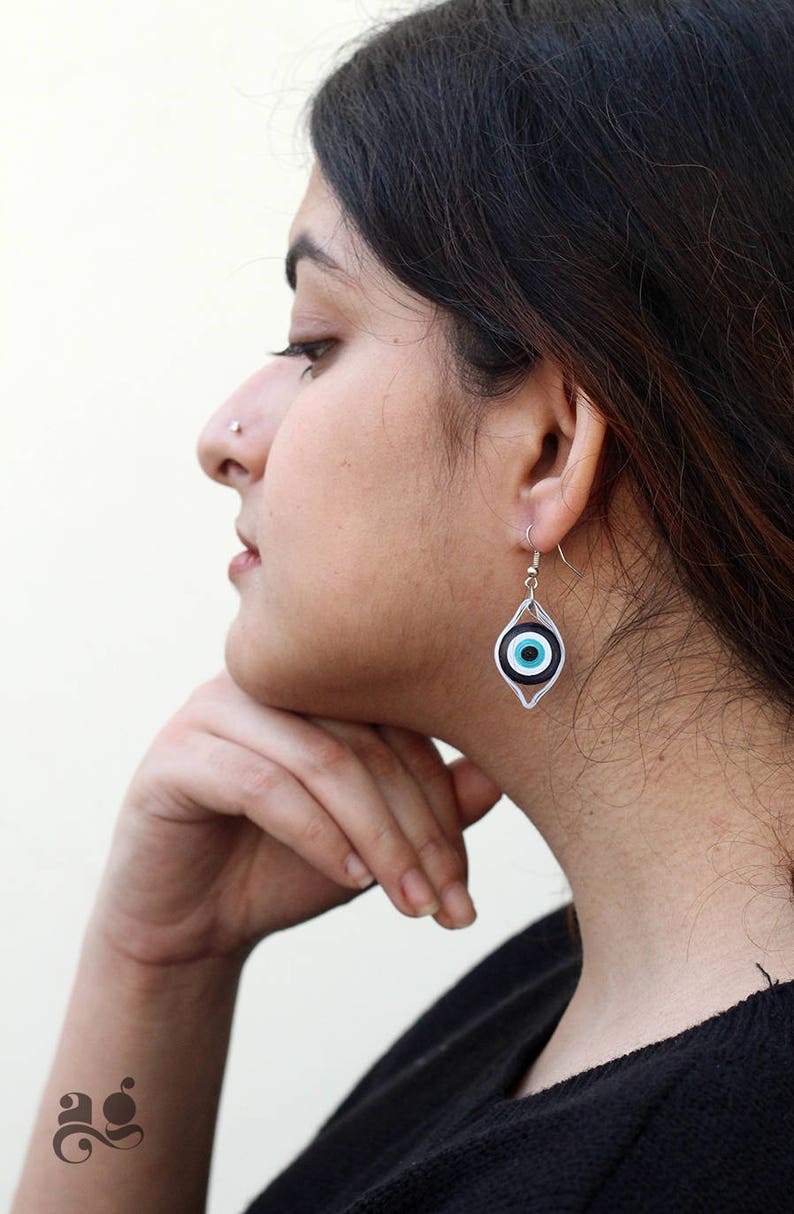 May include: Silver earrings with a blue and black evil eye charm. The earrings are dangling and have a silver hook closure.