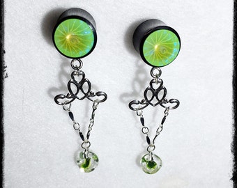 May include: A pair of green and black ear gauges with a dangling chain and a green glass bead at the end. The gauges have a swirl design.