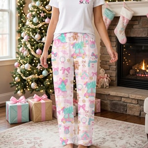 May include: A white short-sleeved t-shirt with the letters SCG in pink and black on the chest, paired with white pajama pants featuring a light pink gingham pattern and a repeating print of Christmas trees, cars, bows, and gingerbread men.
