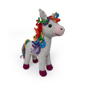 Op de afbeelding: Een gehaakt unicorn speelgoed met een regenboog manen en staart. De unicorn staat op een witte achtergrond.
