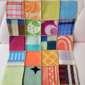 May include: A patchwork blanket made from a variety of colourful squares. The squares display different patterns and textures, such as plaid, floral, and geometric designs. The blanket is stitched together with gold-coloured thread, creating a cosy and unique aesthetic.