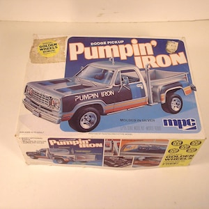 May include: A model kit box for a Dodge Pickup truck, labeled "Pumpin' Iron." The box features a silver and blue truck illustration with the text "Pumpin' Iron." Includes a "Golden Wheels Bonus!" sticker.