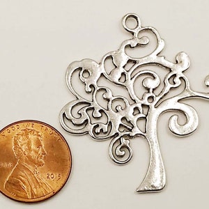 May include: Silver filigree tree charm with a loop at the top for hanging. The charm is about the size of a UK penny.