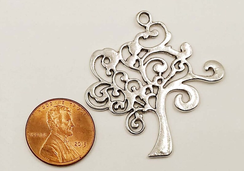 May include: Silver filigree tree charm with a loop at the top for hanging. The charm is about the size of a UK penny.