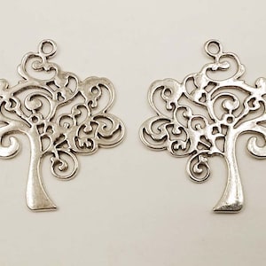 May include: Two silver filigree tree charms with a swirl design. The charms have a hole at the top for hanging.