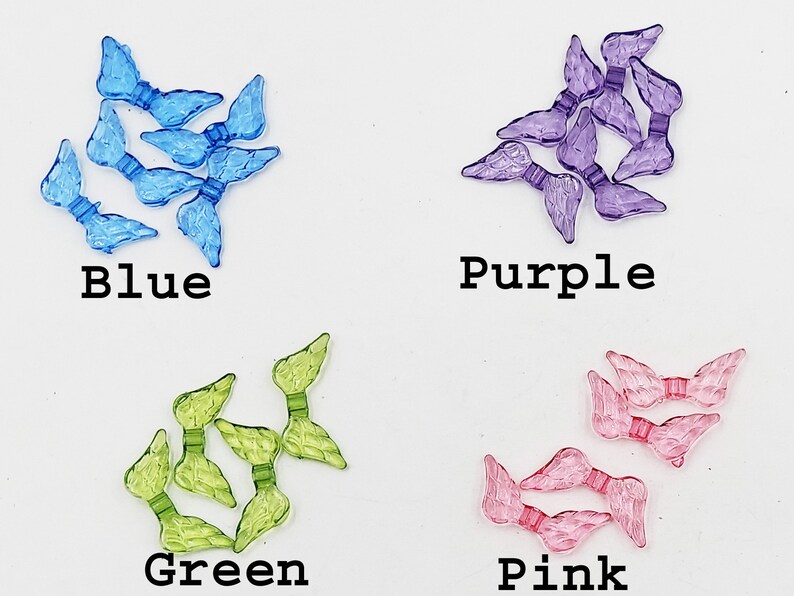 May include: Assortment of plastic angel wings in blue, green, purple, and pink colors. The wings are small and delicate, perfect for crafting or decorating.
