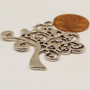 May include: Silver-toned metal tree charm with a detailed, intricate design. The charm is about the size of a UK penny.