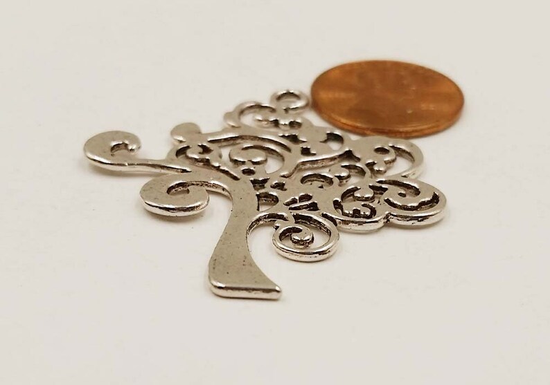 May include: Silver-toned metal tree charm with a detailed, intricate design. The charm is about the size of a UK penny.