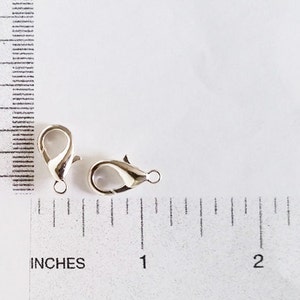 May include: Two silver-toned lobster clasps, each measuring approximately 1 inch in length, are shown against a white background with a ruler for scale.