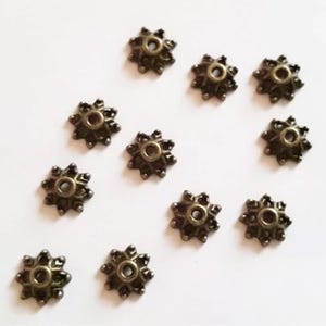 May include: Twelve bronze-colored metal bead caps with a starburst design. Each cap has a small hole in the center.
