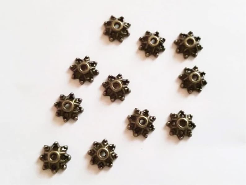 May include: Twelve bronze-colored metal bead caps with a starburst design. Each cap has a small hole in the center.