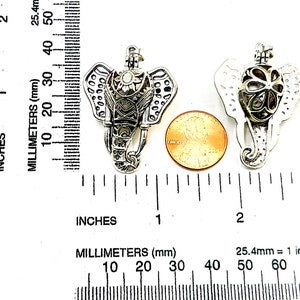May include: Two silver elephant charm pendants with a filigree design. The pendants are about 1 inch in size and are shown next to a US penny for scale.