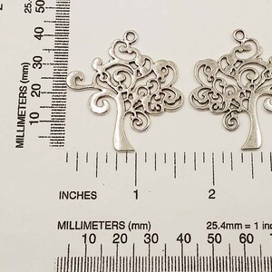 May include: Two silver metal tree charms with intricate filigree designs. The charms are approximately 5 cm in size and have a loop at the top for hanging.