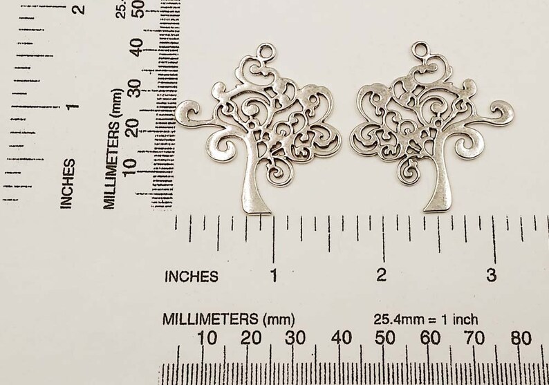 May include: Two silver metal tree charms with intricate filigree designs. The charms are approximately 5 cm in size and have a loop at the top for hanging.