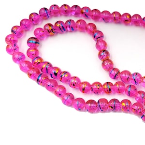 May include: Strands of translucent pink glass beads with colorful, swirled accents. The beads are round and appear to be strung together, creating a necklace or bracelet. The accents include blue, gold, and black colors.