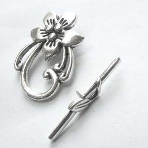 May include: Silver-toned metal toggle clasp with a floral design. The clasp features a decorative flower with a swirl design and a separate, straight bar with a leaf design.