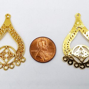 May include: Two gold-colored metal filigree pendant charms, each with a teardrop shape and a smaller circle in the center. The charms are about the size of a US penny.