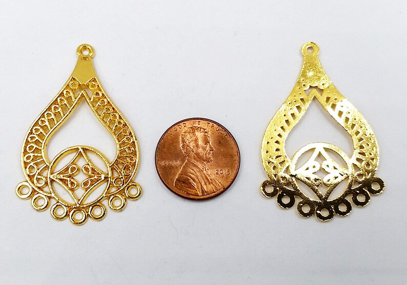 May include: Two gold-colored metal filigree pendant charms, each with a teardrop shape and a smaller circle in the center. The charms are about the size of a US penny.