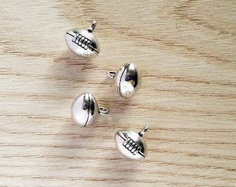 May include: Four silver-toned metal charms shaped like footballs. Each charm has a raised seam down the center and a small loop at the top for attaching to a necklace or bracelet.