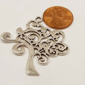 May include: Silver filigree tree charm with a decorative design. The charm is about the size of a UK penny.